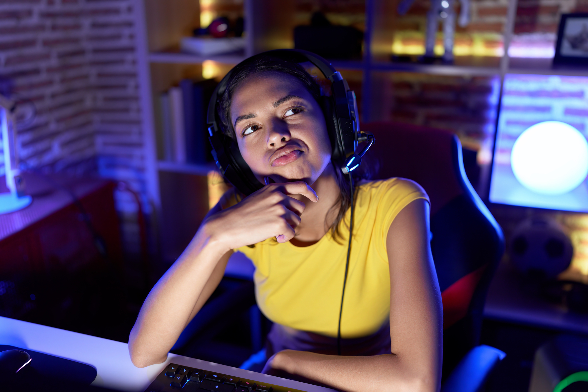Jovem pensativa usando fone de ouvido em frente ao computador onde está jogando online
